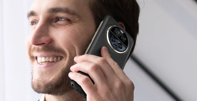 Uomo sorridente con smartphone rugged Ulefone, esemplificante uso quotidiano e robustezza tecnologica.